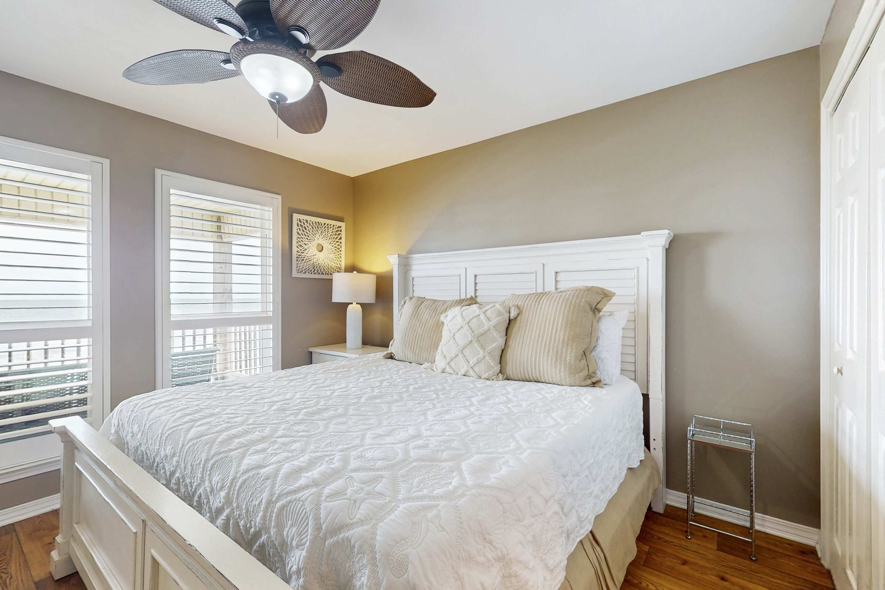 A bedroom with a bed, a ceiling fan, a nightstand, a lamp, and a window with blinds.