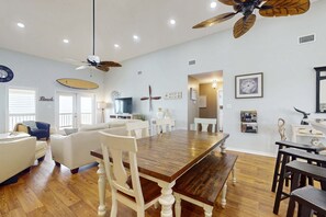 A dining area with a wooden table, white chairs, a ceiling fan, and a television. - Beach Front house with breathtaking views, free WiFi, full kitchen (Dauphin Island)
