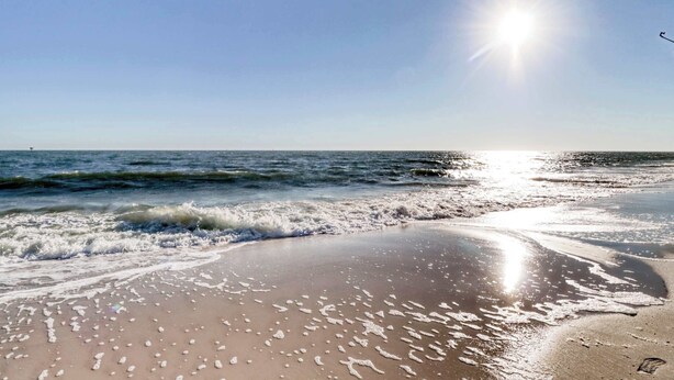 Een strand met golven, een heldere lucht en de zon die schijnt.