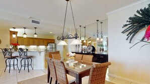 A dining area with wicker chairs, a glass table, and pendant lighting. - Bright beachfront condo with 2 Gulf-side pools, tennis courts & fitness room (Orange Beach)