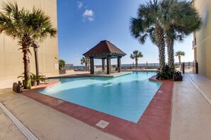 A swimming pool with a gazebo, palm trees, and a view of the beach. - Bright beachfront condo with 2 Gulf-side pools, tennis courts & fitness room (Orange Beach)