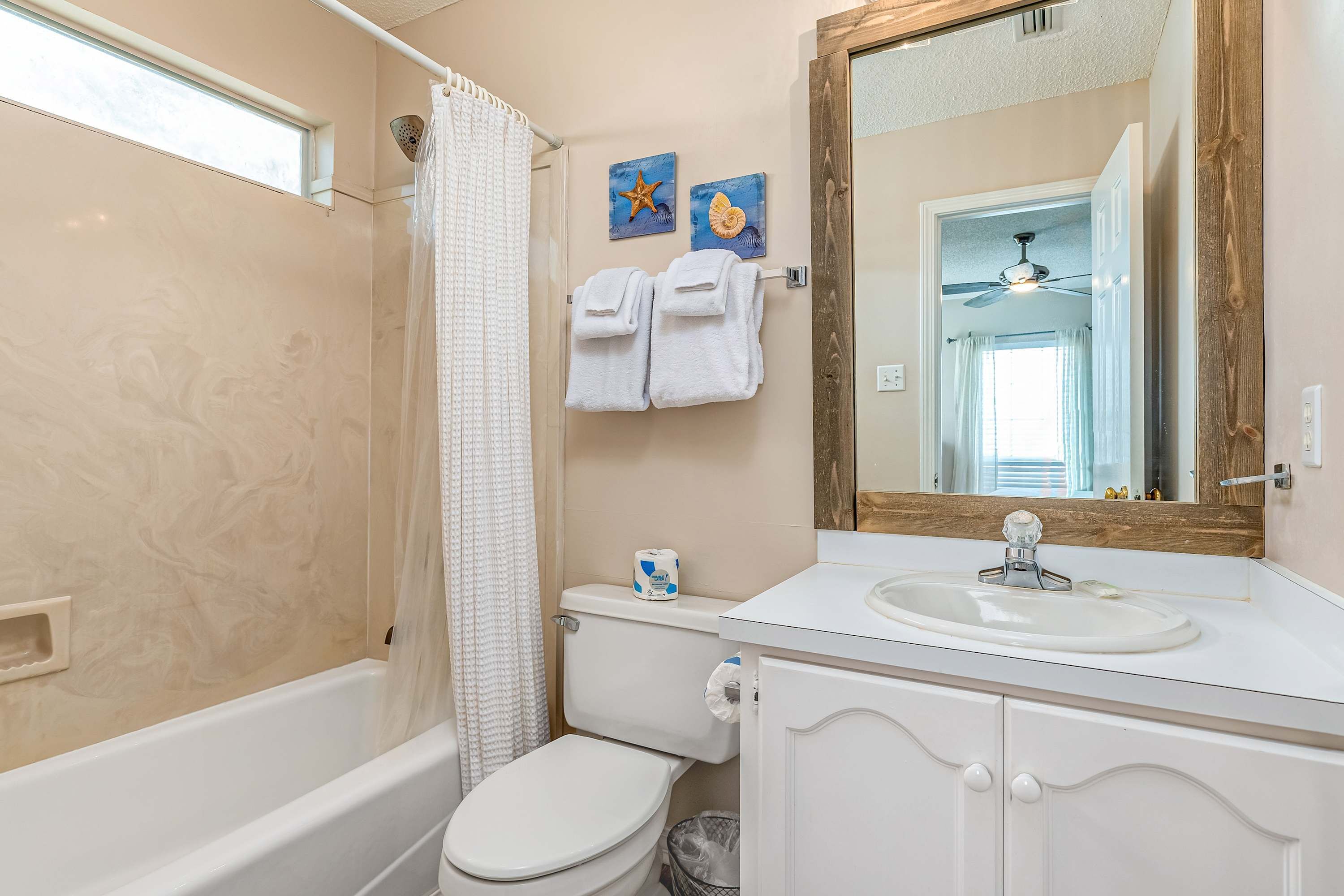 Un bagno con vasca, servizi igienici e lavandino, asciugamani appesi al muro e uno specchio sopra il lavandino.