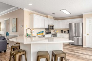 A modern kitchen with white cabinetry, stainless steel appliances, and a central island with stools. - Newly remodeled bay view home with high-speed WiFi, central AC, and gas grill (Dauphin Island)