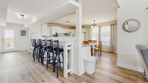 Un vaste espace de vie comprenant une table à manger, des chaises, une cuisine à l’arrière-plan et une grande fenêtre avec des rideaux.