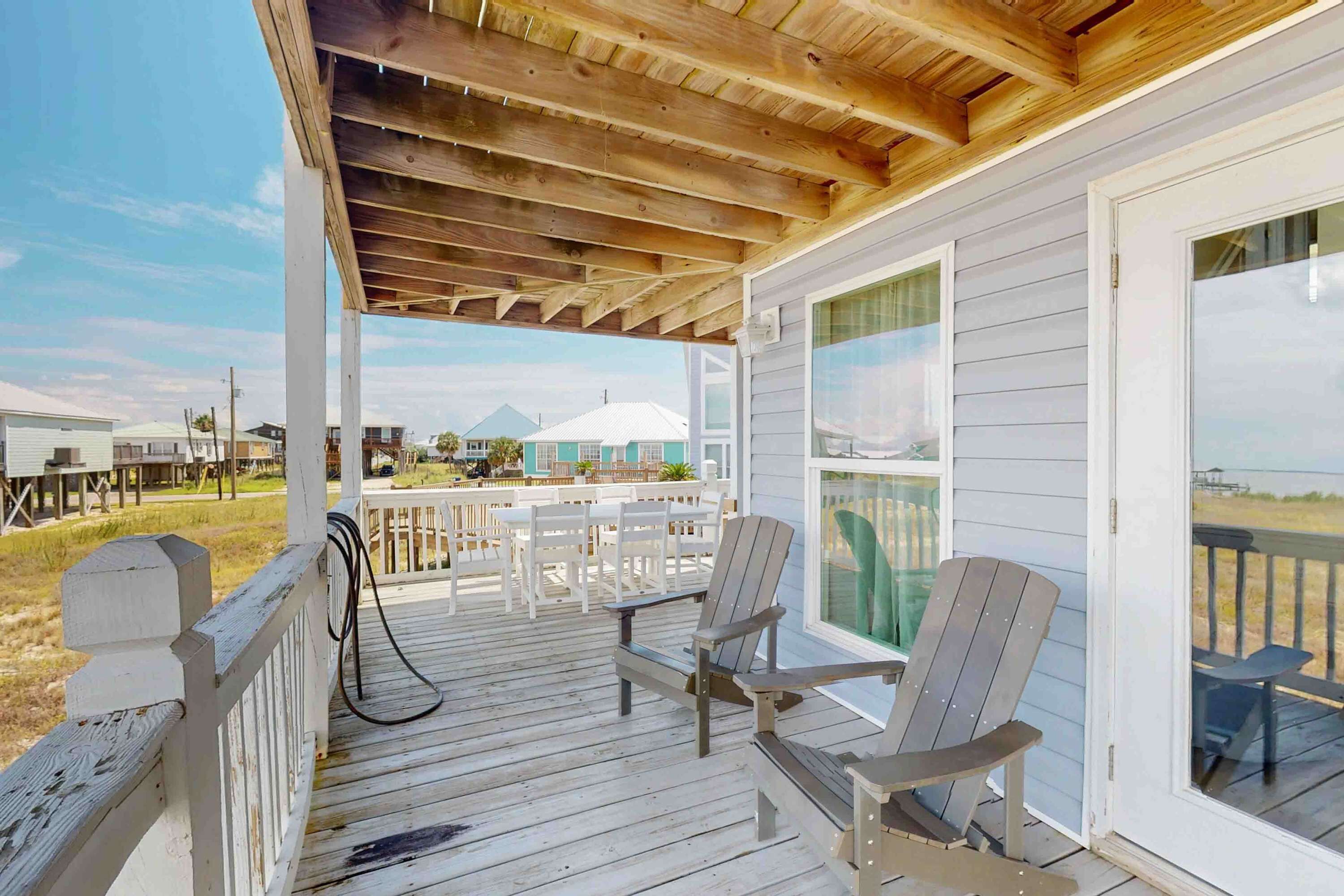 A covered porch with wooden beams, white railings, and two Adirondack chairs.