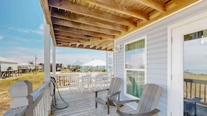 Une véranda couverte avec des poutres en bois, des balustrades blanches et deux fauteuils Adirondack.