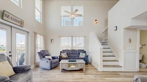 Un salon spacieux avec un plafond haut, un ventilateur de plafond, un escalier et une vue sur l’extérieur.