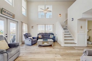 A spacious living room with a high ceiling, a ceiling fan, a staircase, and a view of the outdoors. - Bay Front Home with - Gulf Views, WiFi, & Washer/Dryer - Two Dogs Welcome (Dauphin Island)