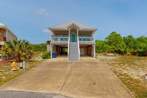 A two-story house with a front porch, a staircase leading to the entrance, and a concrete driveway. - Spacious Island Gem Near the Beach & Town With Large Deck & Pool - Dogs OK (Dauphin Island)