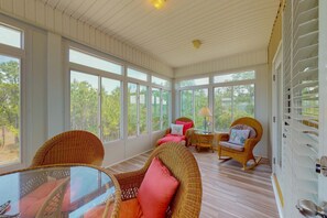 A sunlit room with large windows, wicker furniture, and a glass table. - Spacious Island Gem Near the Beach & Town With Large Deck & Pool - Dogs OK (Dauphin Island)