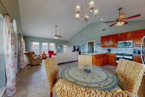 A spacious living area with a round glass-top table, wicker chairs, a ceiling fan, and wooden cabinets. - Spacious Island Gem Near the Beach & Town With Large Deck & Pool - Dogs OK (Dauphin Island)