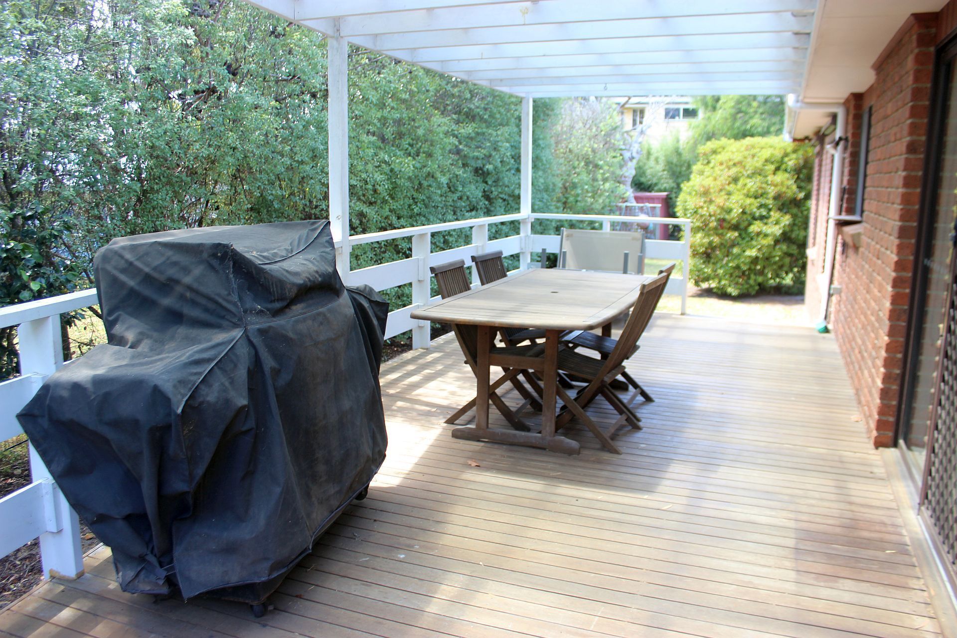 A covered patio with a wooden table and chairs, a grill, and a white railing.