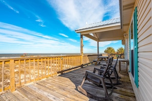 Una terraza de madera con mobiliario exterior, una zona cubierta y vista a la playa y al océano.