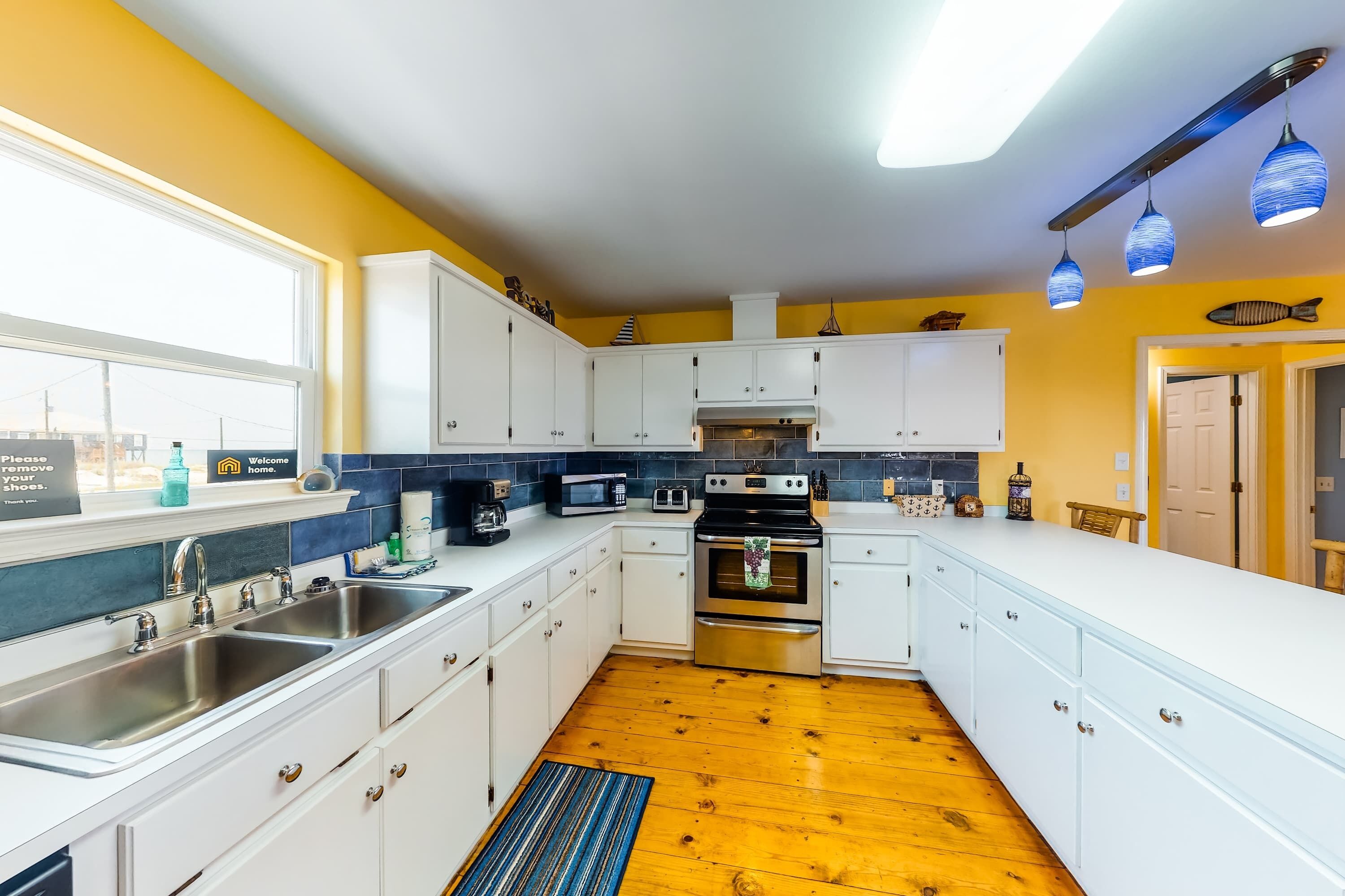 A modern kitchen with white cabinets, stainless steel appliances, a wooden floor, and a view of the outside.