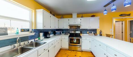 A modern kitchen with white cabinets, stainless steel appliances, a wooden floor, and a view of the outside.
