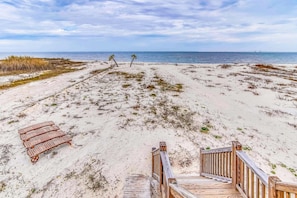 Ein Strand mit einer Holzterrasse, einer Palme und einer entfernten Brücke.