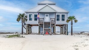 Una casa frente a la playa con balcón, una escalera que lleva a la entrada y vista al océano.