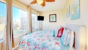 Een slaapkamer met een bed, een plafondventilator, een televisie en kunst aan de muur.