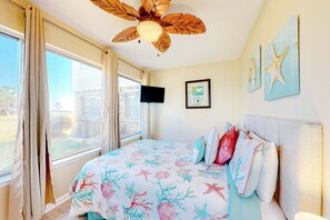 A bedroom with a bed, a ceiling fan, a TV, and artwork on the wall. - Quiet home with WiFi, pool, view of water, & boardwalk to beach (Dauphin Island)