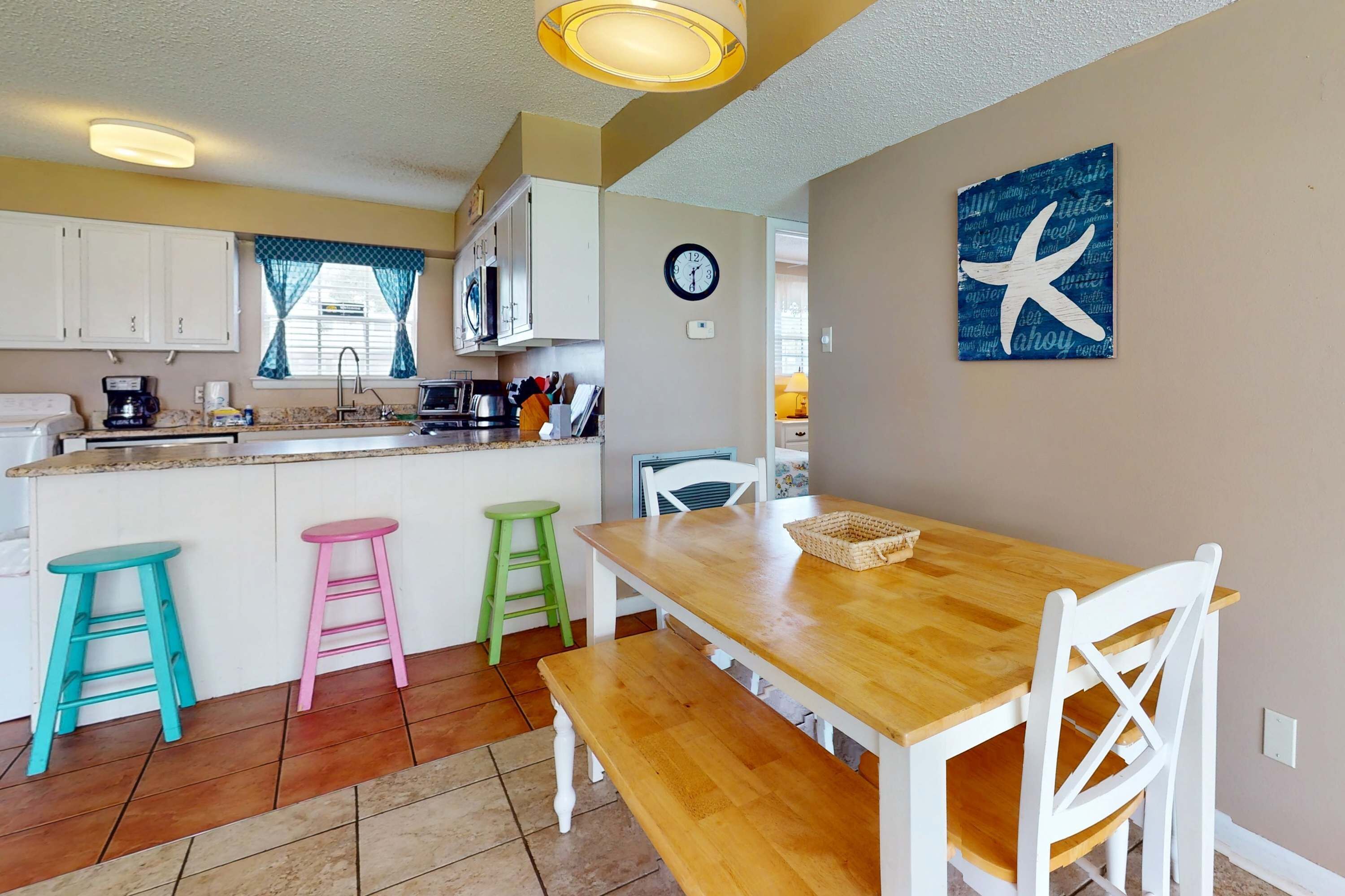 Una cocina con armarios blancos, una mesa de comedor de madera con sillas blancas y una obra de arte con forma de estrella de mar en la pared.