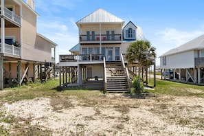 A multi-story beachfront house with a balcony, wooden deck, and a staircase leading to the upper level. - Charming bay-front home with WiFi, spacious wraparound porch, private deck (Dauphin Island)