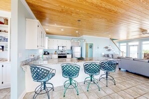 A modern kitchen with white cabinets, a marble countertop, and a central island with bar stools. - Charming bay-front home with WiFi, spacious wraparound porch, private deck (Dauphin Island)