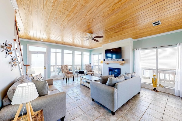 A spacious living room with a high ceiling, a fireplace, and a large window. - Charming bay-front home with WiFi, spacious wraparound porch, private deck (Dauphin Island)