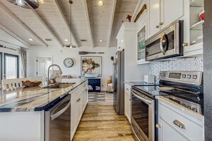 A kitchen with white cabinetry, stainless steel appliances, a wooden floor, and a large island with a sink. - Charming beachfront home with Gulf views & wraparound deck - right on the sand (Dauphin Island)