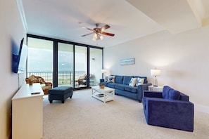 A living room with a sofa, ottoman, coffee table, and a ceiling fan. - Beachfront condo with pool, private balcony, and washer and dryer (Dauphin Island)