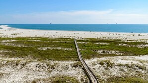 Une plage avec une promenade en bois qui mène à l’eau, des dunes de sable et un ciel dégagé.