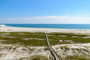 A beach with a wooden boardwalk leading to the water, sandy dunes, and a clear sky. - Beachfront condo with pool, private balcony, and washer and dryer (Dauphin Island)