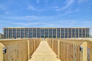 A wooden boardwalk leading to a multi-story hotel with a flat roof and numerous windows. - Beachfront condo with pool, private balcony, and washer and dryer (Dauphin Island)