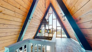 Ein Holzinnenraum mit schrägen Decken, einer Treppe und Blick durch ein Fenster.