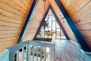 A wooden interior with a sloped ceiling, a staircase, and a view through a window. - Unique beachside A-frame with porches, fantastic views & ocean access (Dauphin Island)