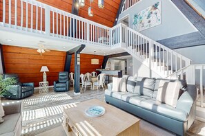 A spacious living area with a high ceiling, a staircase, and a view of the kitchen. - Unique beachside A-frame with porches, fantastic views & ocean access (Dauphin Island)