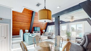 Ein geräumiges Wohnzimmer mit einem Glastisch, bequemen Sitzgelegenheiten, einer großen Holzwand und einem Deckenventilator.