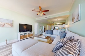 A living room with a sofa, a coffee table, a TV, and a ceiling fan. - Beachfront condo with pool, private balcony, and laundry (Dauphin Island)