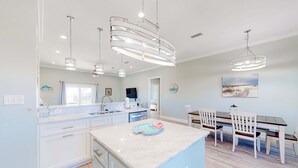 Una cucina moderna con mobili bianchi, un'isola in marmo e illuminazione a sospensione.