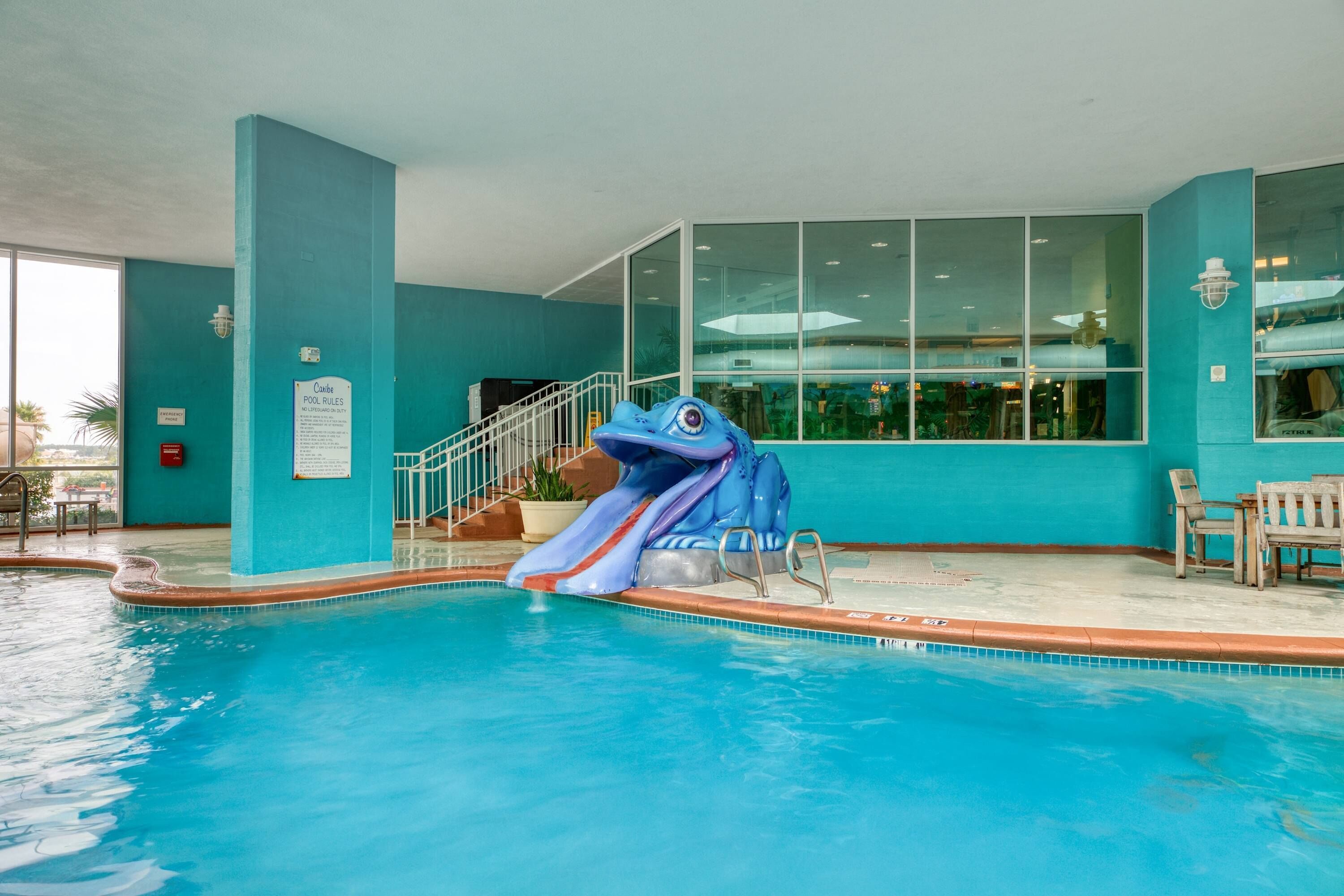 An indoor pool with a blue slide, a staircase, and a view of the outside.