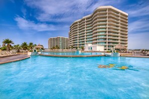 A hotel with a large swimming pool, palm trees, and a thatched-roof structure. - Beachview condo with lazy river, marina, multiple pools and internet (Orange Beach)
