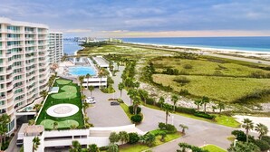 A hotel with a pool, a tennis court, and a view of the beach and ocean. - Beachview condo with lazy river, marina, multiple pools and internet (Orange Beach)
