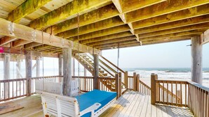 Une terrasse en bois avec un lit, un escalier et une vue sur l’océan.