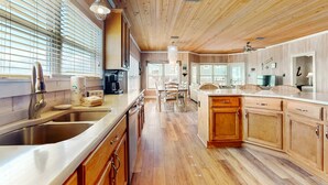 Eine moderne Küche mit Holzschränken, einer Edelstahl-Spüle und einem Essbereich mit Tisch und Stühlen.
