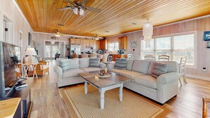 Ein geräumiges Wohnzimmer mit Holzboden, ein großes, graues Ecksofa, ein Couchtisch und eine Küche im Hintergrund.