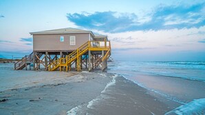 Una casa de playa con terraza de madera y escaleras que conducen a la entrada.