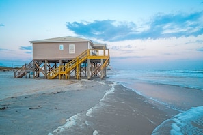 Une maison de plage dotée d’une terrasse en bois et d’un escalier menant à l’entrée.