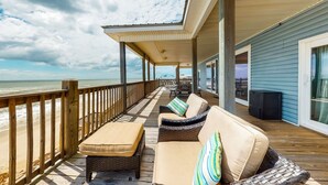 Eine überdachte Terrasse mit Gartenmöbeln, einem Holzwert und Blick auf den Strand.