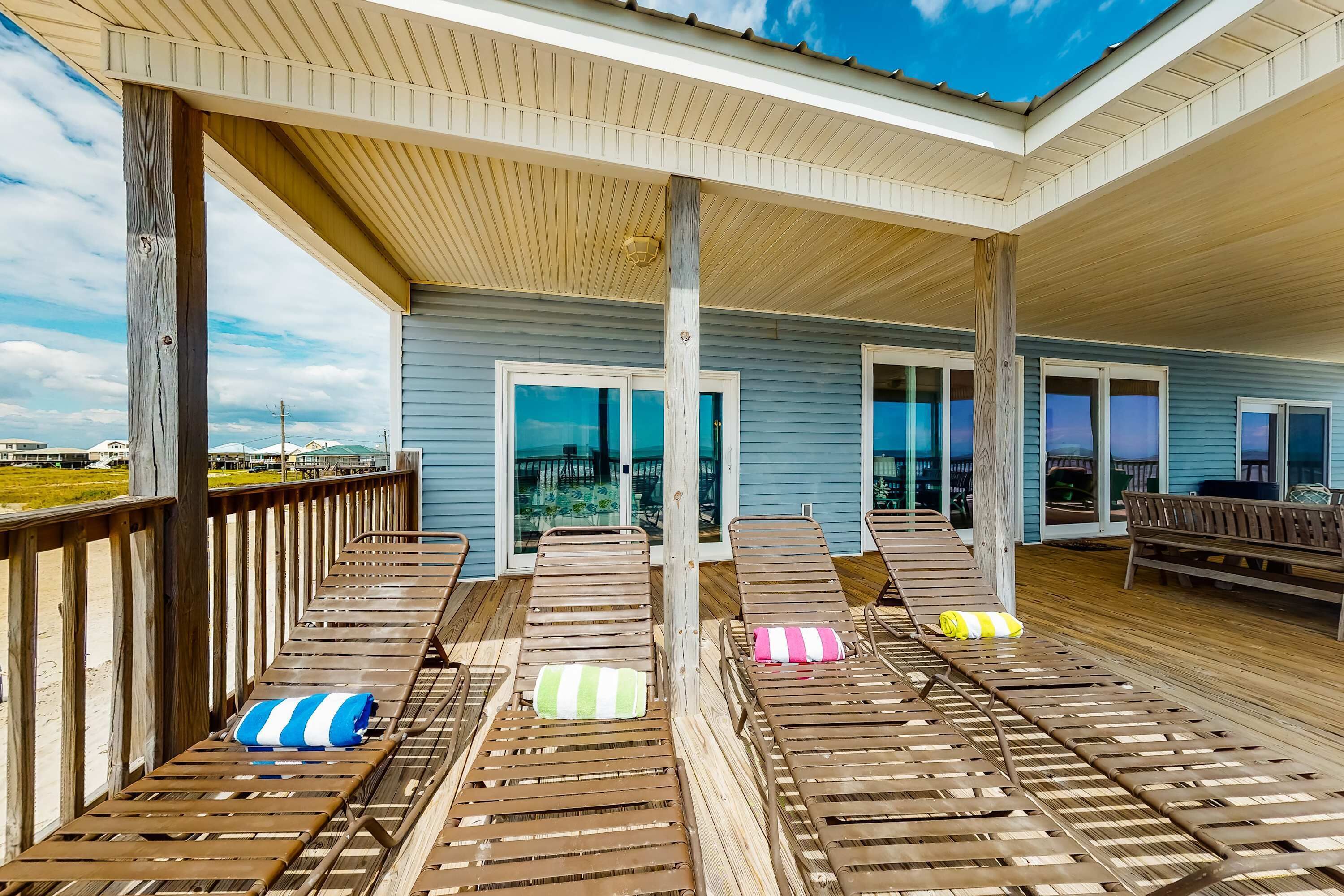 A covered deck with wooden lounge chairs and a view of the beach.