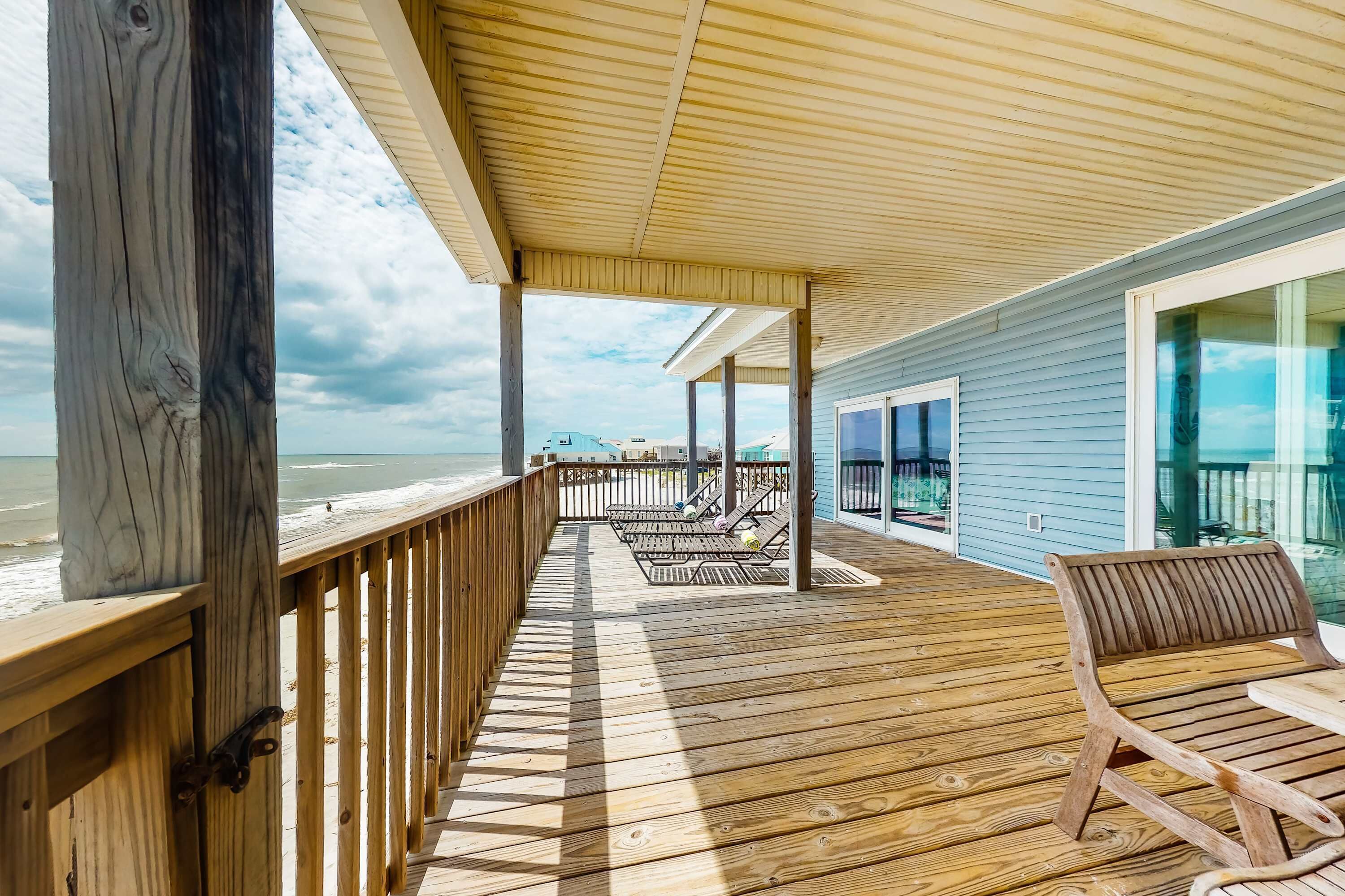Un terrazzo in legno con poltrone da relax, una ringhiera e vista sulla spiaggia.