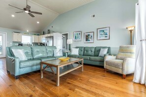 A living room with a sofa, a coffee table, a patterned armchair, and a ceiling fan. - Dog-friendly seaside home with WiFi, deck, amazing views, minutes from beach (Dauphin Island)